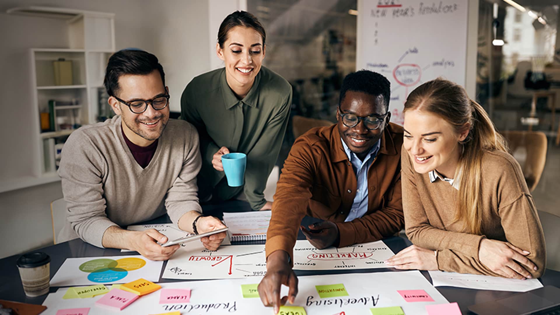 A group of four individuals collaborates over a table filled with colorful papers and charts, engaged in a team discussion.