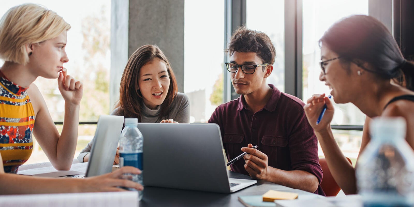 Four students sitting around a laptop screen in discussion.